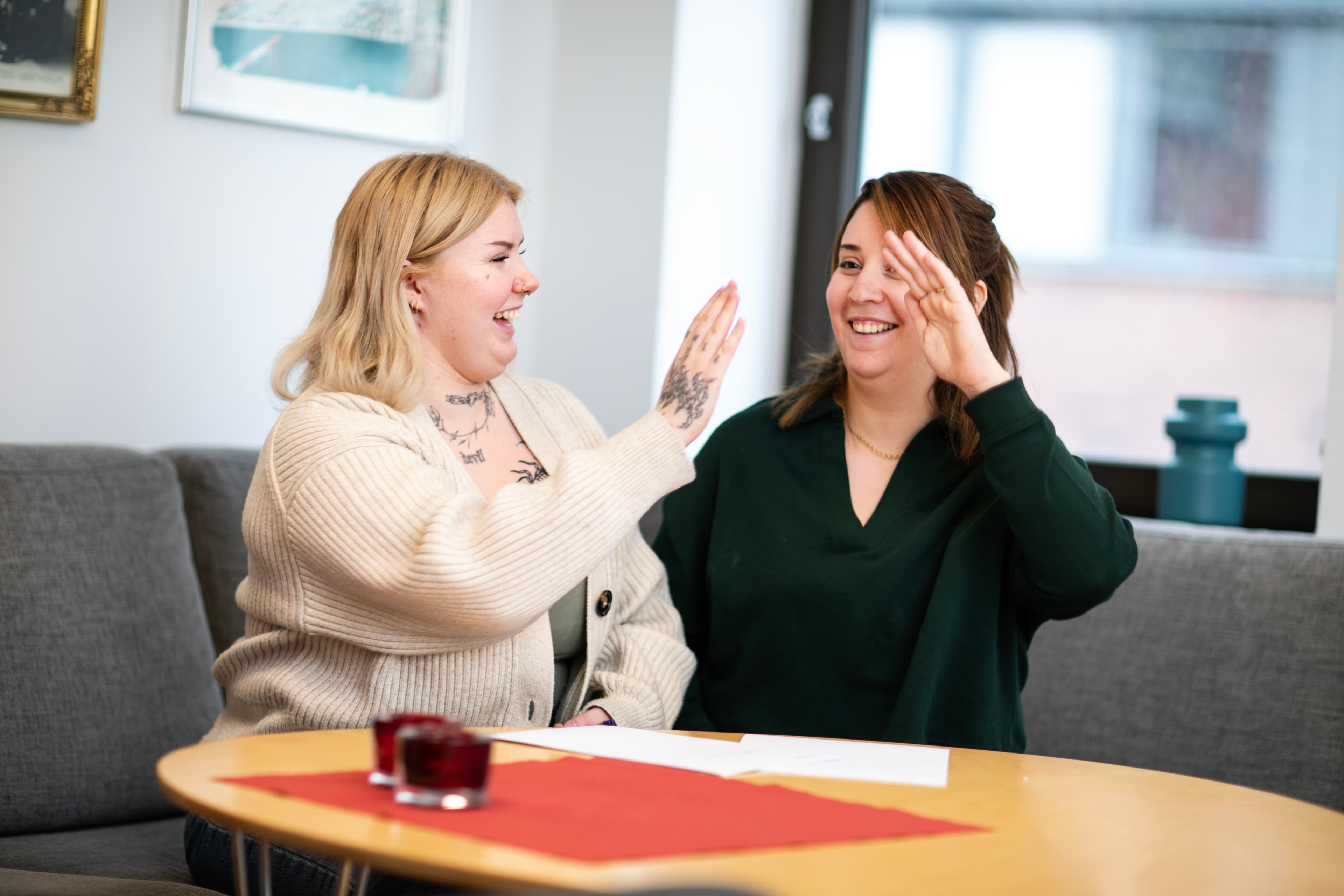 Två kvinnor sitter i en soffa och ger varandra en high five.